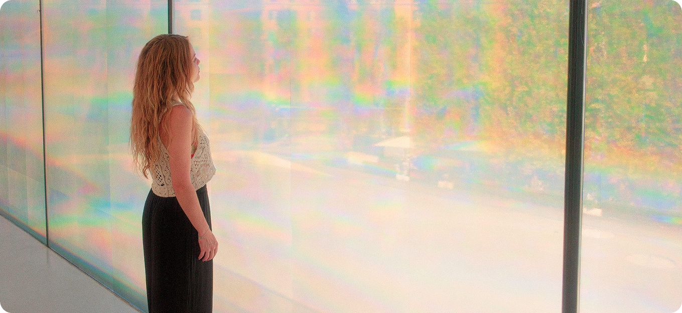 Frau blickt auf eine schimmernde, in Regenbogenfarben spielende Glaswand